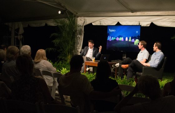 Three people sitting on a stage with a small audience 